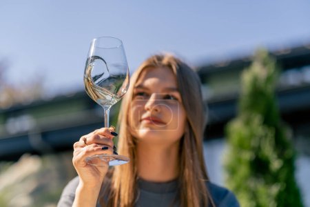 Téléchargez les photos : Gros plan d'une belle fille tenant un verre de vin à la main, inhalant son arôme et le dégustant sur la terrasse du jardin - en image libre de droit