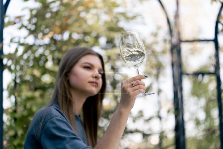 Foto de Una chica pensativa se sienta en un hermoso arco en el jardín con una copa de vino degustándolo cuidadosamente - Imagen libre de derechos