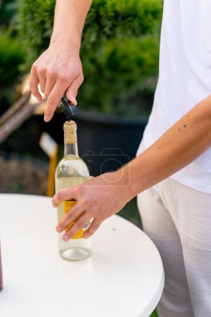 Foto de Primer plano de la mano de un sommelier masculino usando un sacacorchos para desenroscar el corcho de madera de una botella de vino - Imagen libre de derechos