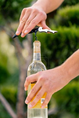 Téléchargez les photos : Gros plan de la main d'un sommelier masculin à l'aide d'un tire-bouchon pour dévisser le bouchon en bois d'une bouteille de vin - en image libre de droit