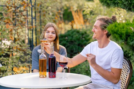 Téléchargez les photos : Un couple de gars et une fille sont assis ensemble à une table dans le jardin d'une cave et déguster différents types de vin - en image libre de droit