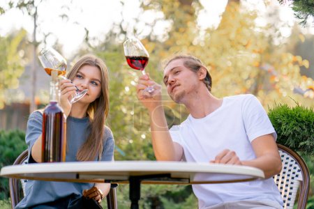 Foto de Una pareja de un chico y una chica están sentados juntos en una mesa en el jardín de una bodega y degustando diferentes tipos de vino - Imagen libre de derechos