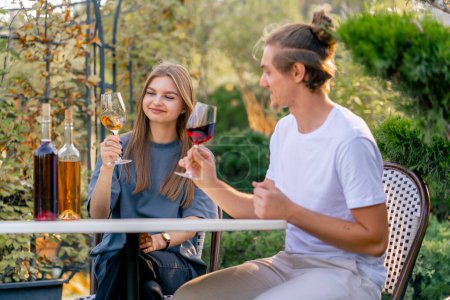 Foto de Una pareja de un chico y una chica están sentados juntos en una mesa en el jardín de una bodega y degustando diferentes tipos de vino - Imagen libre de derechos