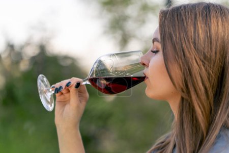 Photo for Side view close-up shot of a young girl drinking aged wine from a beautiful glass in nature - Royalty Free Image