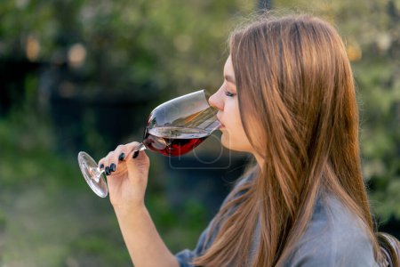 Téléchargez les photos : Vue latérale gros plan d'une jeune fille buvant du vin vieilli dans un beau verre dans la nature - en image libre de droit