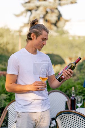 Téléchargez les photos : Sommelier professionnel masculin prépare une bouteille de vin pour la dégustation aux invités dans le jardin de la cave - en image libre de droit