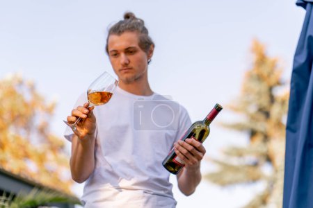 Téléchargez les photos : Sommelier professionnel masculin prépare une bouteille de vin pour la dégustation aux invités dans le jardin de la cave - en image libre de droit