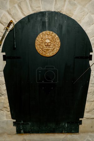 Téléchargez les photos : Décoration dorée faite à la main en forme de soleil sur de grandes portes en bois à l'entrée de la cave souterraine - en image libre de droit