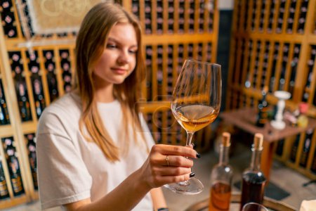 Photo for A beautiful girl holds a glass of wine in her hand and checks its quality during a tasting in a wine cellar - Royalty Free Image