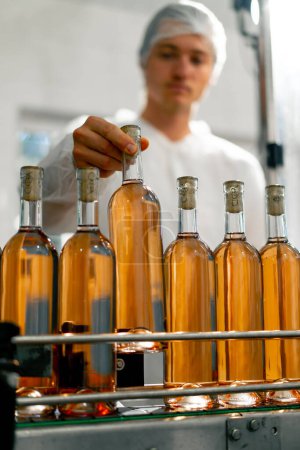 Foto de Un tecnólogo masculino controla el proceso de envasado y distribución de botellas de vino en producción - Imagen libre de derechos