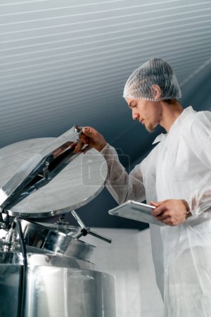 Foto de Primer plano de un tecnólogo profesional con una tableta en una fábrica de alimentos que abre un tanque para controlar la producción - Imagen libre de derechos