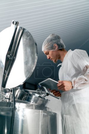 Téléchargez les photos : Gros plan d'un technologue professionnel avec une tablette dans une usine alimentaire ouvrant un réservoir pour contrôler la production - en image libre de droit