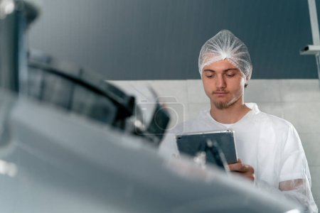 Foto de Primer plano de un tecnólogo profesional con una tableta en una fábrica de alimentos que abre un tanque para controlar la producción - Imagen libre de derechos