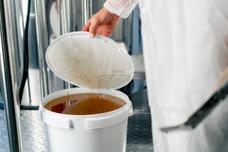 Foto de La mano de un tecnólogo abre un barril de miel líquida natural para ser añadido a la producción de bebidas - Imagen libre de derechos