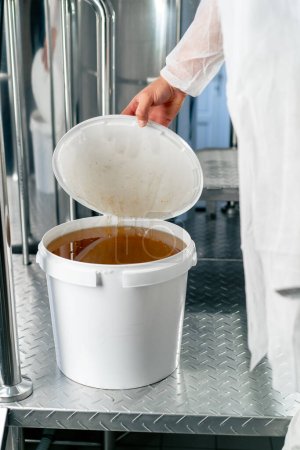 Photo for The hand of a technologist opens a barrel of natural liquid honey to be added to the production of drinks - Royalty Free Image