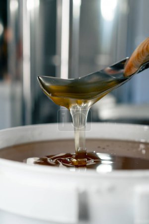 Foto de Primer plano de una cuchara de metal revolviendo miel líquida natural que fluye de nuevo en un tazón grande - Imagen libre de derechos