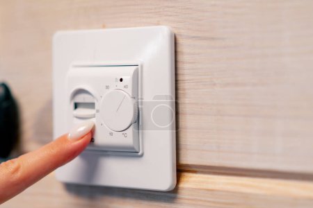 Foto de La mano de la mujer enciende el botón para calefacción por suelo radiante y ajusta la temperatura del calor en él - Imagen libre de derechos