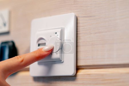 Foto de La mano de la mujer enciende el botón para calefacción por suelo radiante y ajusta la temperatura del calor en él - Imagen libre de derechos