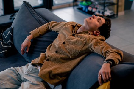Téléchargez les photos : Un jeune homme s'est endormi assis sur le canapé avec la télécommande à la main et regardant la télévision - en image libre de droit