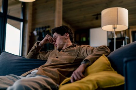 Téléchargez les photos : Un jeune homme s'est endormi assis sur le canapé avec la télécommande à la main et regardant la télévision - en image libre de droit