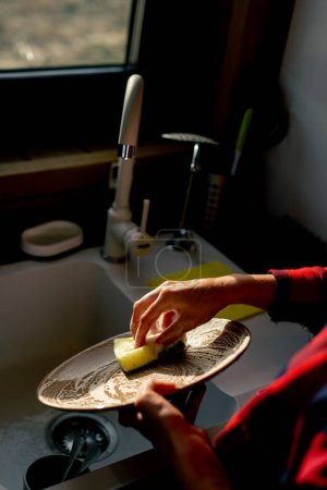 Foto de Primer plano de la mano de una mujer con una esponja de espuma lavar platos bajo la presión del agua en una cocina - Imagen libre de derechos