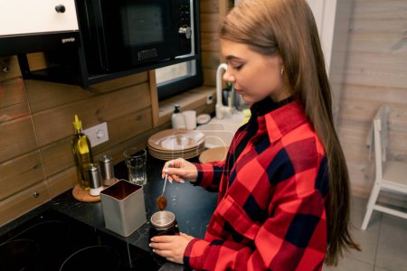 Téléchargez les photos : Une jeune fille prépare un café tôt le matin dans une turbine geyser dans la cuisine de sa maison - en image libre de droit