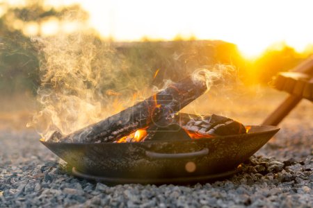 Photo for Close-up shot of a fire with wood burning at sunset near a cosy wooden house in the countryside - Royalty Free Image
