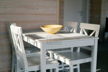 Photo for The rays of the sun illuminate a light table and several chairs that stand in a spacious kitchen in wooden house - Royalty Free Image