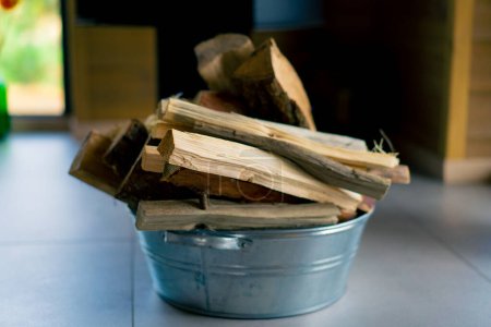Téléchargez les photos : Une pile de bois de chauffage coupé pour allumer une cheminée se trouve dans un seau de fer dans une maison de campagne - en image libre de droit