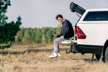 Téléchargez les photos : Un gars est assis dans le coffre d'une voiture tout en voyageant à travers de beaux endroits dans la forêt et la steppe - en image libre de droit