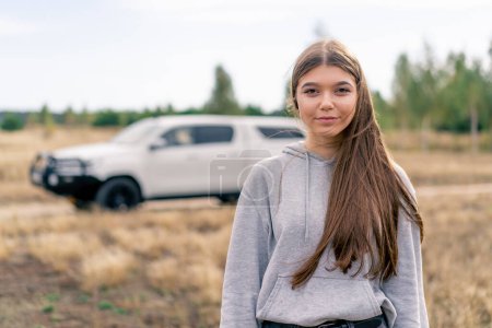 Photo for A beautiful girl stands in a field against the backdrop of car before a trip through the forest - Royalty Free Image