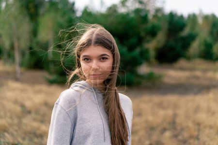 Téléchargez les photos : Portrait d'une belle jeune fille aux cheveux longs debout dans un champ sur fond de pins - en image libre de droit