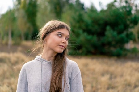 Téléchargez les photos : Portrait d'une belle jeune fille aux cheveux longs debout dans un champ sur fond de pins - en image libre de droit