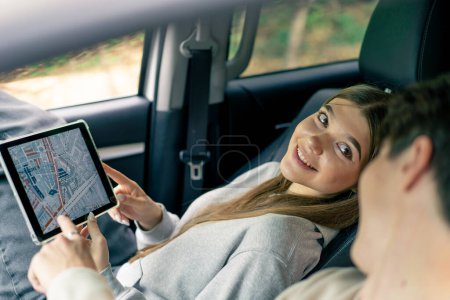 Photo for A couple in a car conferring and planning the best route through the forest using a map on tablet - Royalty Free Image