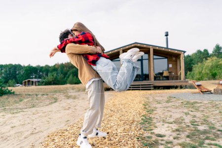 Téléchargez les photos : Un jeune homme tourne sa bien-aimée fille dans ses bras dans la rue à l'extérieur de la maison de campagne - en image libre de droit