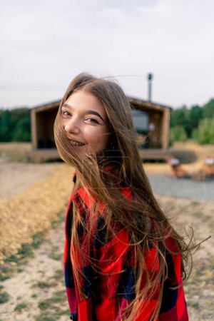 Foto de Retrato de cerca de la cara de una hermosa chica que corre a la cabaña de madera en el bosque y mira hacia atrás - Imagen libre de derechos