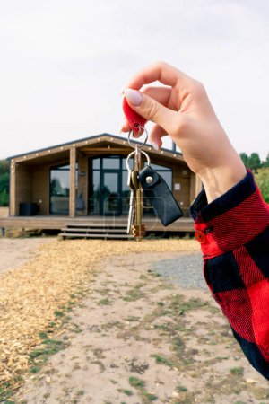 Téléchargez les photos : Gros plan de la main d'une femme tenant les clés de sa maison de campagne en bois récemment achetée dans un bois - en image libre de droit