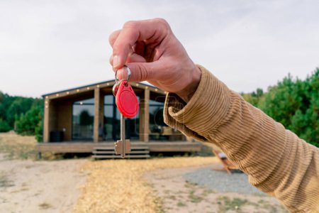 Photo for Close-up shot of a man's hand holding the keys to his newly purchased suburban wooden house in a woods - Royalty Free Image
