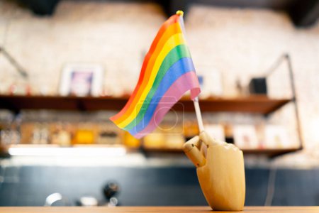 Photo for Close-up shot of a stand in the form of a wooden hand holding a rainbow small flag of lgbt representatives on the background of a wooden store - Royalty Free Image