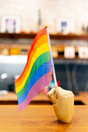 Foto de Primer plano de un soporte en forma de una mano de madera sosteniendo una pequeña bandera de arco iris de representantes lgbt en el fondo de una tienda de madera - Imagen libre de derechos