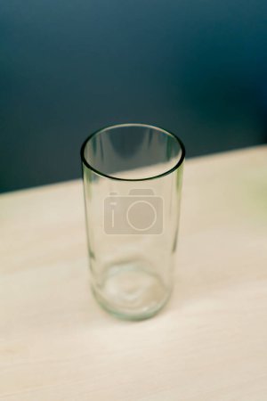 Téléchargez les photos : Un verre en verre transparent coloré se tient vide sur une table en bois dans un magasin de décoration à la main - en image libre de droit