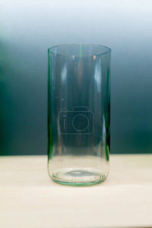 Foto de Un vaso de vidrio hecho de vidrio transparente de color se encuentra en una mesa de madera en una tienda de decoración hecha a mano - Imagen libre de derechos