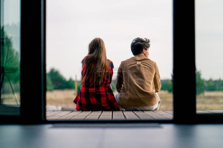 Téléchargez les photos : Plan arrière d'un homme et d'une fille assis sur la terrasse d'une maison en bois et admirant la nature de la steppe et de la forêt - en image libre de droit