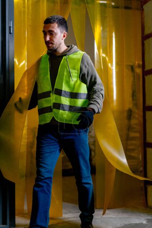 Foto de Un empleado de la estación de reciclaje de residuos con un chaleco de trabajo camina a través de una cortina de silicona en la puerta de la planta - Imagen libre de derechos