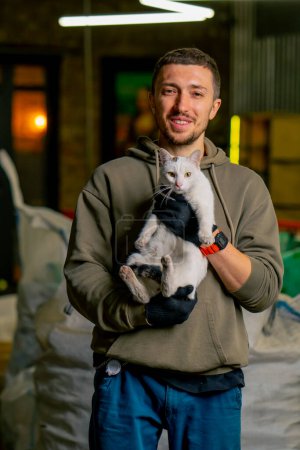 Photo for Portrait of a worker at a waste recycling station holding a local beautiful cat in his arms and smiling - Royalty Free Image