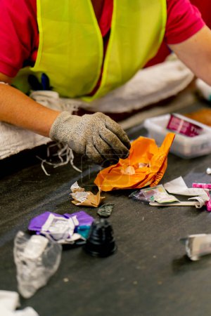 Foto de Primer plano de las manos femeninas en guantes de trabajo clasificando la basura en categorías en una línea especial en una fábrica - Imagen libre de derechos