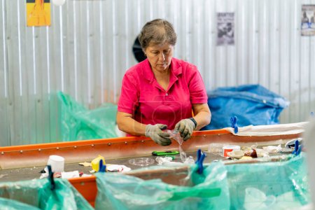 Foto de Una mujer mayor seria trabaja en una estación de reciclaje de residuos y clasifica la basura para su posterior procesamiento - Imagen libre de derechos