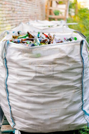 Téléchargez les photos : Un grand sac lourd avec une énorme quantité de bouteilles en verre usagées est préparé pour leur élimination dans une station de recyclage des déchets - en image libre de droit