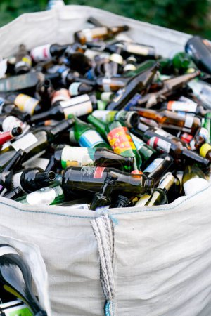 Foto de Una gran bolsa pesada con una gran cantidad de botellas de vidrio usadas se prepara para su eliminación en una estación de reciclaje de residuos - Imagen libre de derechos