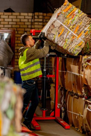 Foto de Un empleado masculino que usa un apilador saca una caja de papel con artículos usados para ser transportados y enviados para su reciclaje - Imagen libre de derechos